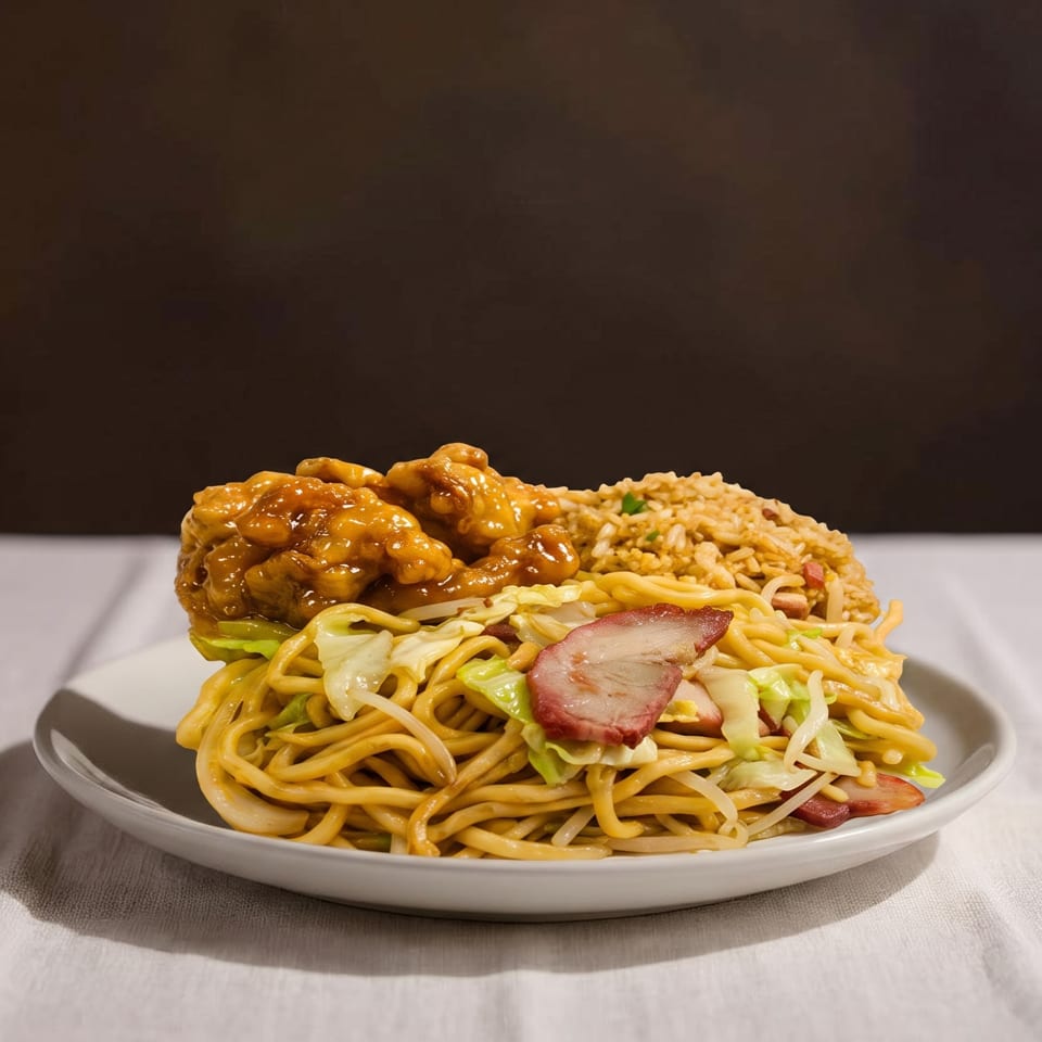 Plate of chow mein noodles with roast pork, fried rice, and saucy chicken on a white tablecloth.