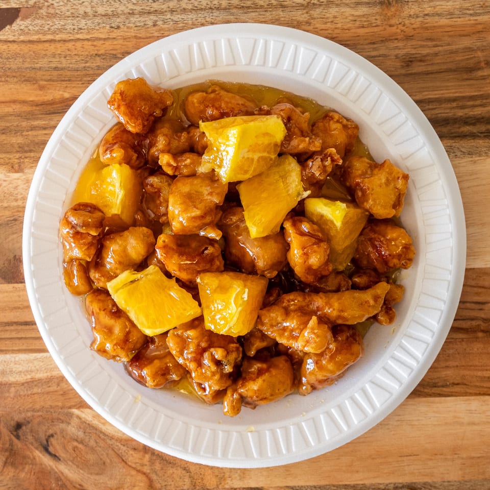 Crispy battered chicken pieces and orange chunks coated in glossy sauce, served on a white plate atop a wooden table.