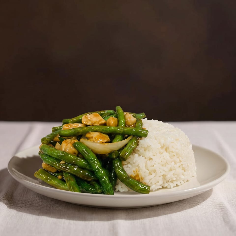 Plate of stir-fried green beans, chicken, and onions with a mound of white rice.